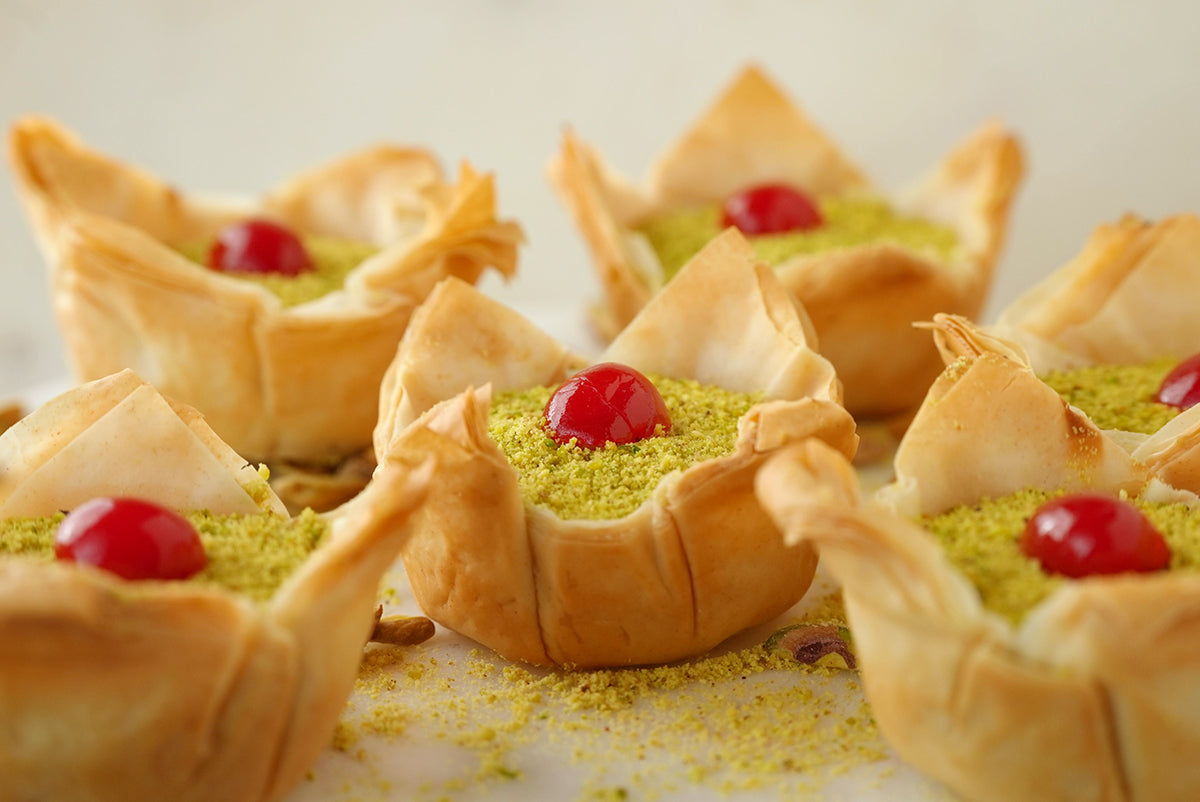 Several Sogarina Creste, our baklava cheesecake, set side by side on a white counter dusted with pistachio.